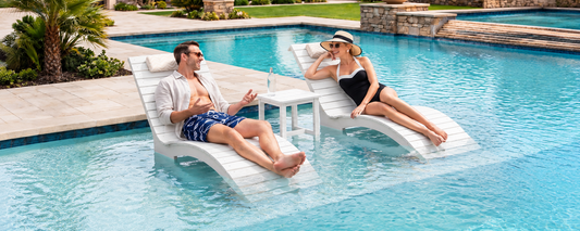 A couple relaxing on matching AquaCurve Aquawave in-pool lounge chairs with a side table on a shallow sun shelf